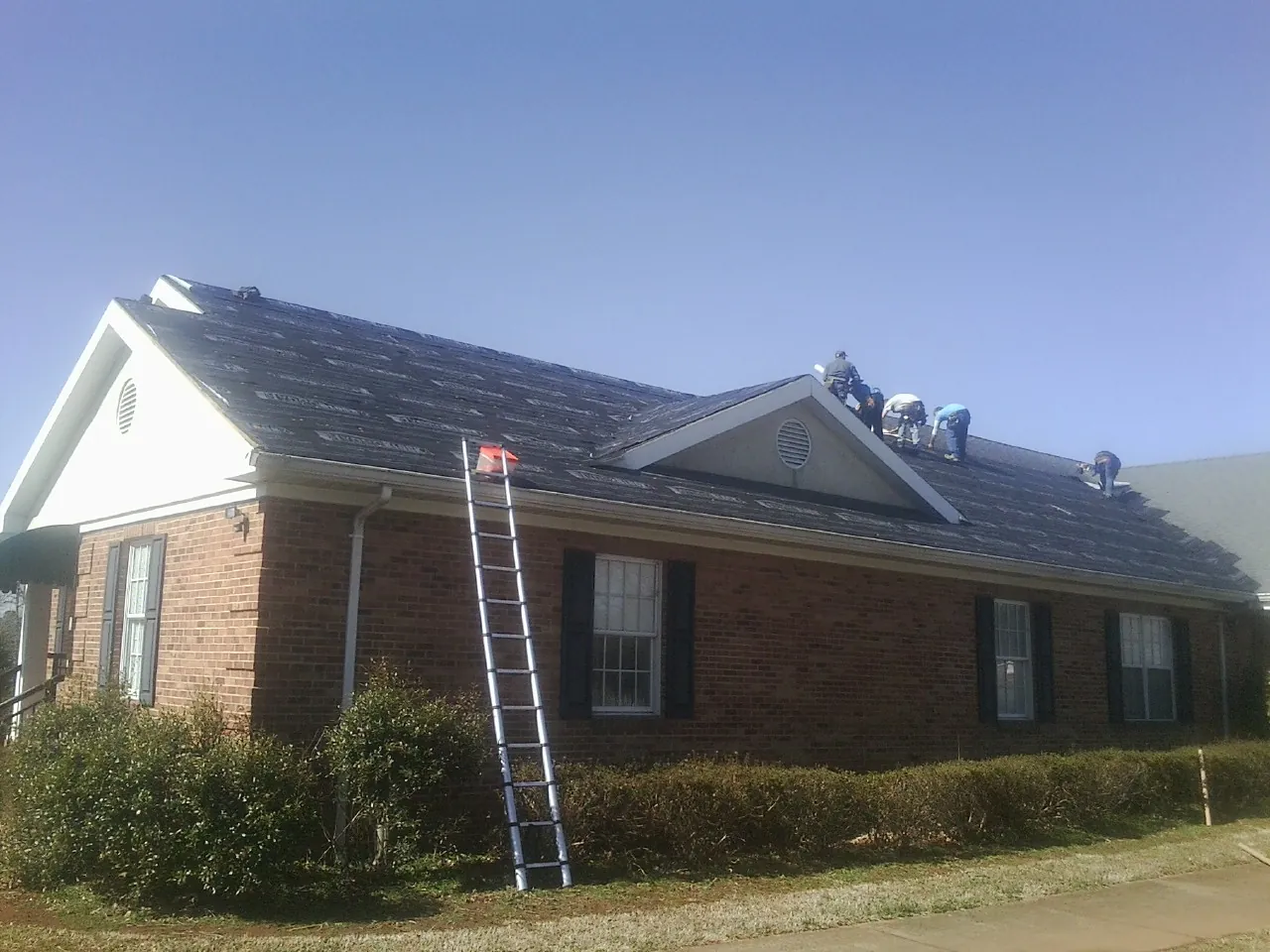 Crew tearing shingles off a brick ranch roof with a ladder set — Emergency Roof Repair work by our crew in Everson