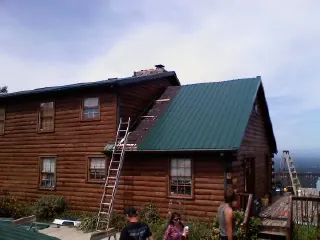 Green metal roof going on a two story log home with ladders set in Everson