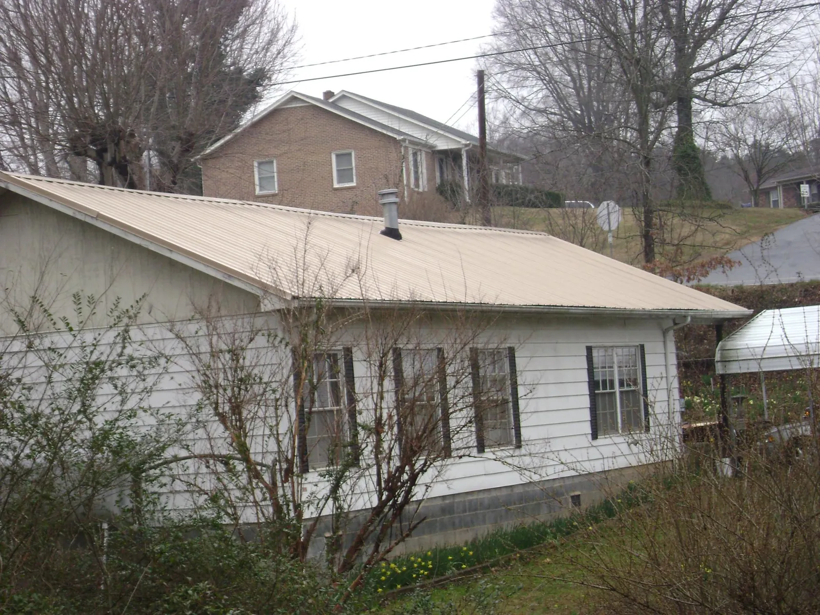 Tan metal roof on a white sided house set into a hillside — Commercial Roofing by Roofing Brothers in Everson